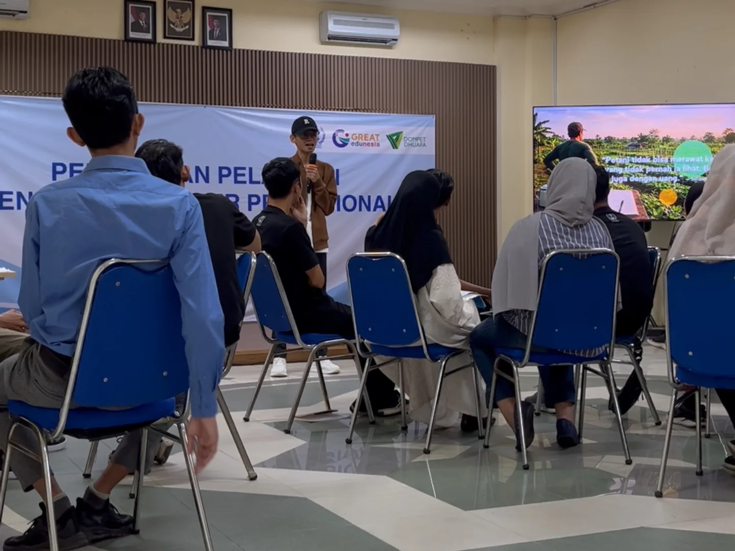 Instruktur Setiawan Chogah memberikan materi literasi finansial Merawat Kebun Rezeki kepada peserta pelatihan Barber, Menjahit, dan Bright Migrant Worker di ruang kelas Institut Kemandirian, Karawaci, Tangerang, dengan presentasi ilustrasi kebun rezeki ditampilkan di layar.