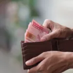Seseorang memegang dompet berisi uang rupiah sebagai ilustrasi pengelolaan keuangan dan konsep Lega Finansial.