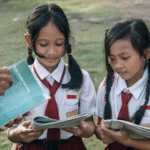 Dua siswa sekolah dasar di Indonesia sedang belajar bersama guru sebagai ilustrasi artikel tentang gratifikasi di sekolah dan pentingnya integritas dalam dunia pendidikan.