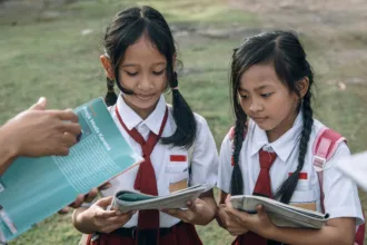 Dua siswa sekolah dasar di Indonesia sedang belajar bersama guru sebagai ilustrasi artikel tentang gratifikasi di sekolah dan pentingnya integritas dalam dunia pendidikan.