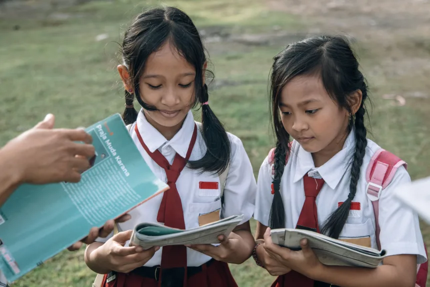 Dua siswa sekolah dasar di Indonesia sedang belajar bersama guru sebagai ilustrasi artikel tentang gratifikasi di sekolah dan pentingnya integritas dalam dunia pendidikan.